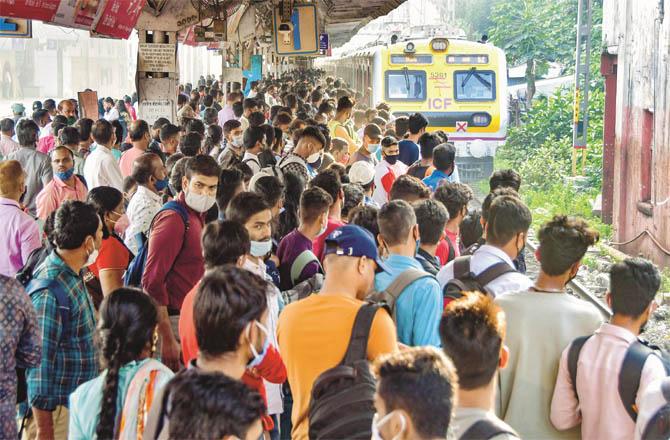 At a railway station in the city, passengers stand ready to board a local train