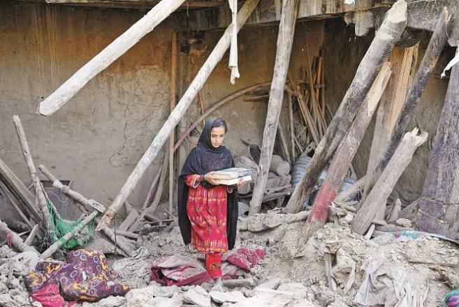 A girl with books on the rubble of a mud house in a village in Gyan District.Picture:AP/PTI