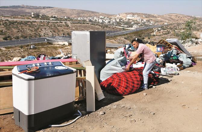 A Palestinian with belongings after a house was demolished in occupied Beit al-Maqdis.