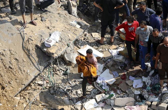 A Palestinian carries the body of a child wrapped in a blanket from the rubble. Photo: PTI