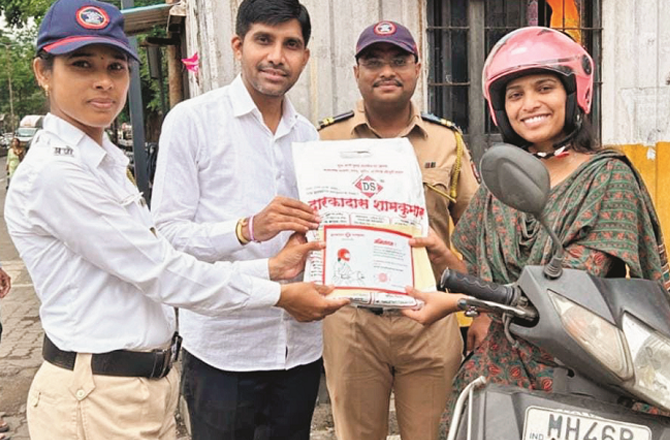 A woman riding a scooter is being given a saree for wearing a helmet. Photo: INN