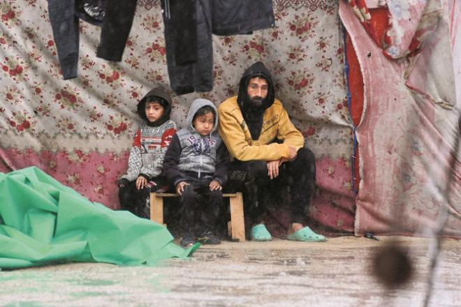 A father sits with his children under a tent during the rain in a refugee camp in Gaza. Photo: INN