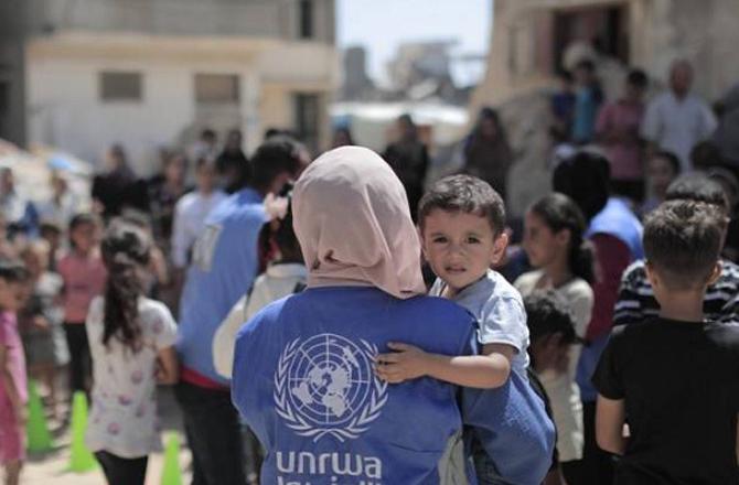 A UNRWA worker holds a child in her arms. Photo: INN