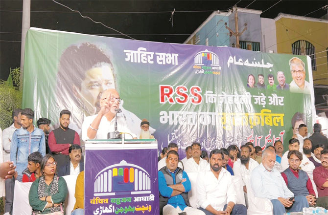 In the picture, Niranjan Takle is giving a speech and other important participants are sitting on the stage.