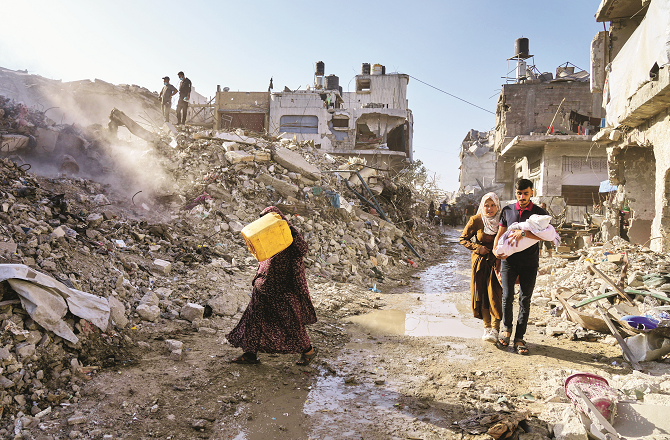 Palestinians walk through rubble in Gaza. Photo: AP/PTI Palestinians walk through rubble in Gaza. Photo: AP/PTI